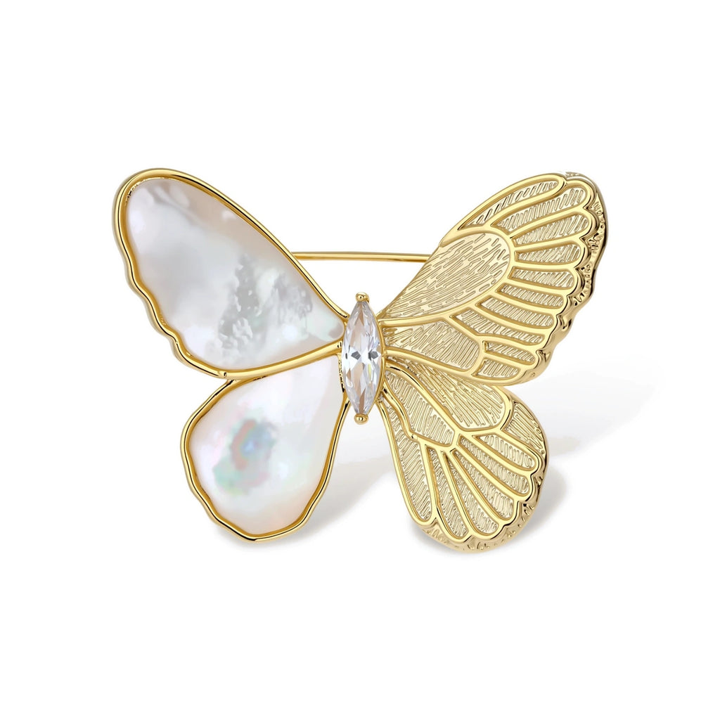 Gold-plated butterfly brooch with mother-of-pearl left wings, engraved gold right wings, and central zirconia crystal on cream background.