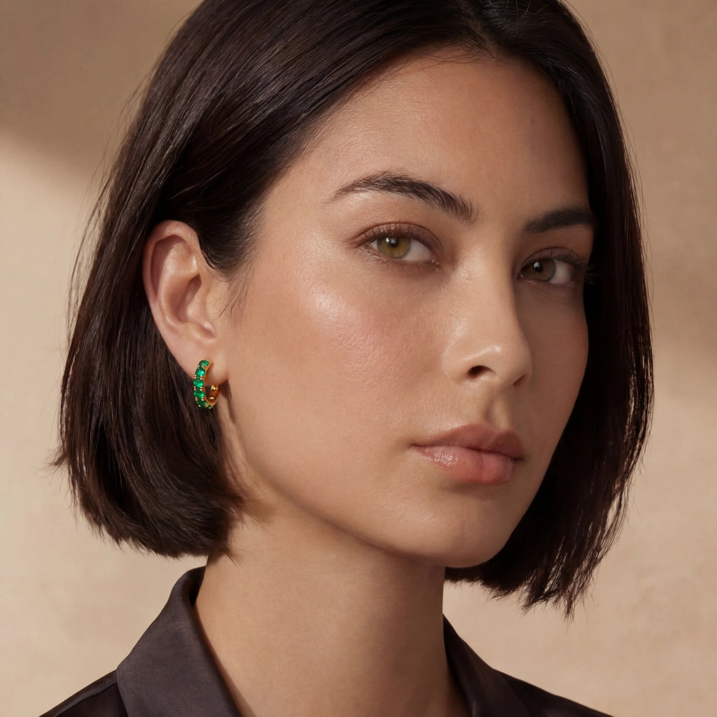 Close-up of a woman with short dark hair wearing green earrings against a beige background