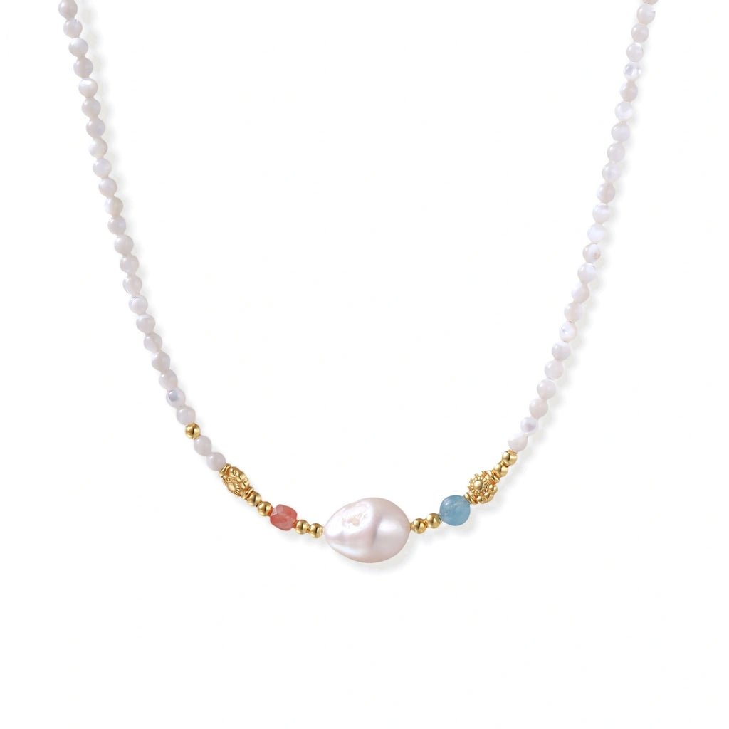 Delicate white beaded necklace with baroque pearl center, gold accents, and coral and aqua gemstones on cream background.