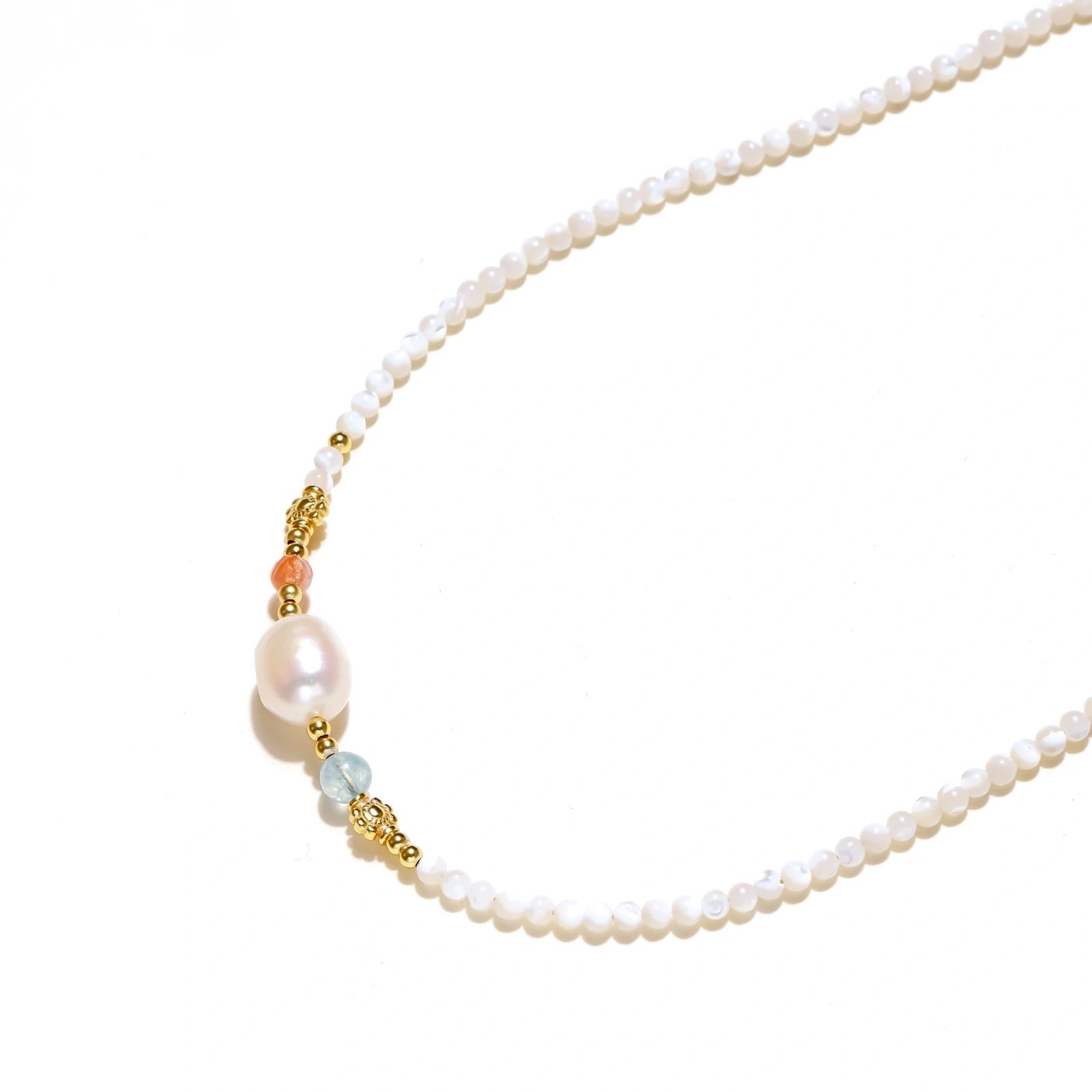 Delicate white beaded necklace with baroque pearl center, gold accents, and coral and aqua gemstones on cream background.
