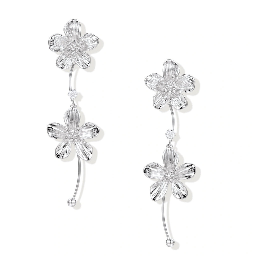 Silver-white asymmetric earrings with textured flower petals and crystal centers on cream background