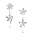 Silver-white asymmetric earrings with textured flower petals and crystal centers on cream background