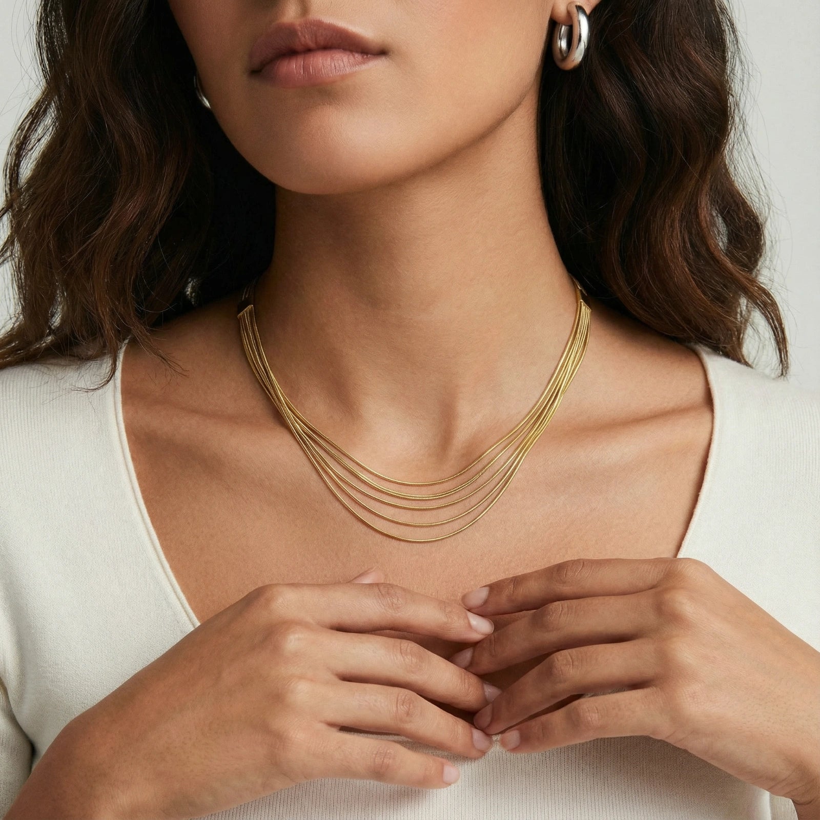 Woman in white shirt wearing a layered golden necklace.