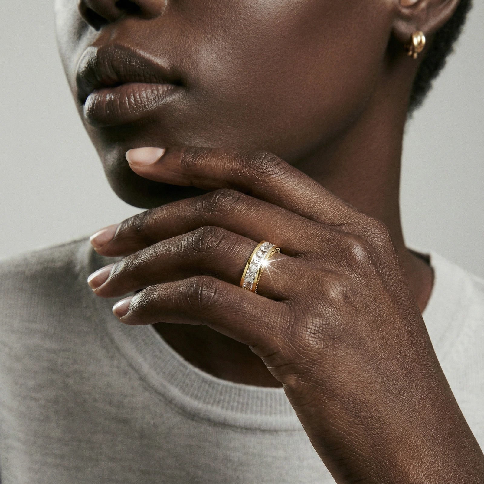 Close-up of a person wearing a gold ring on a neutral background
