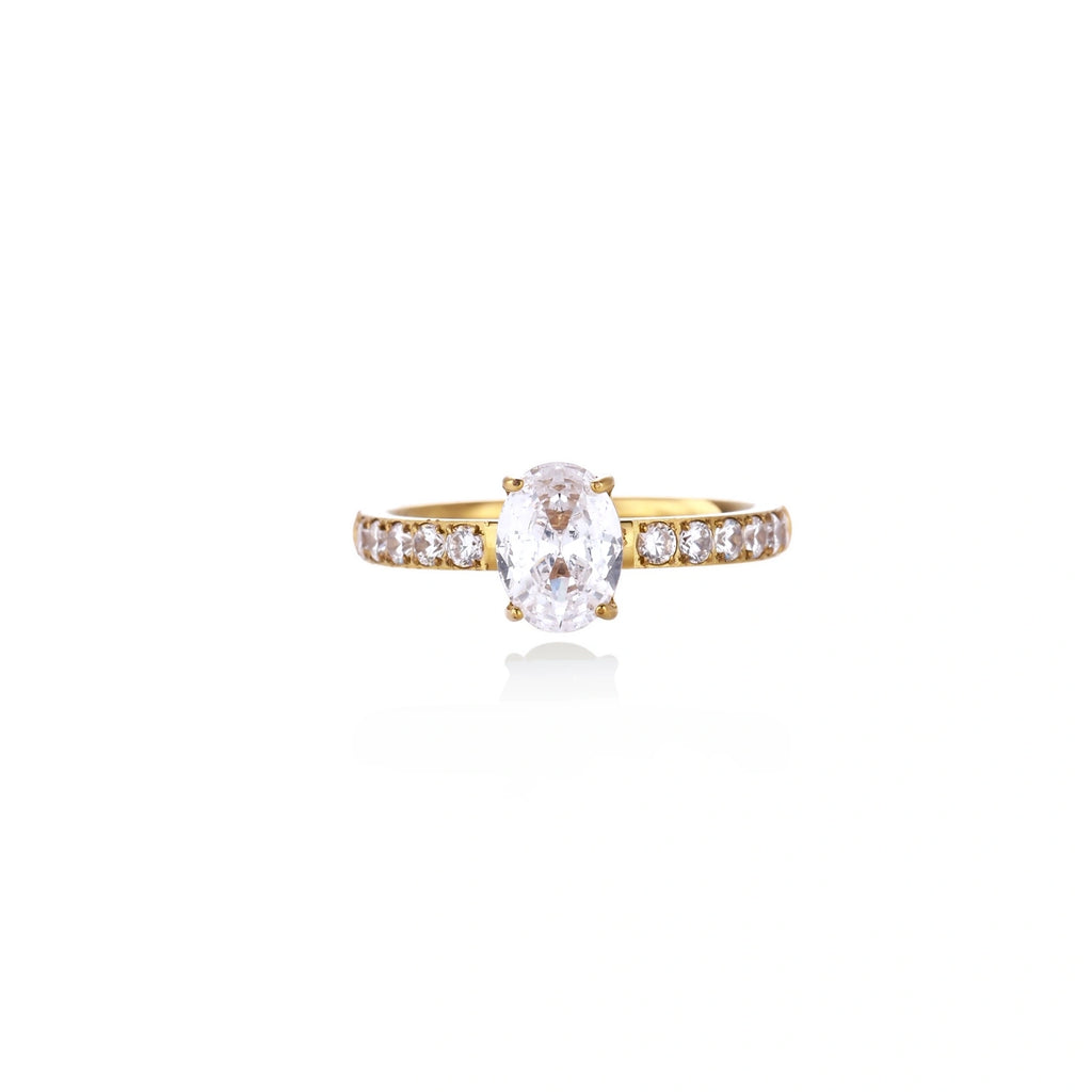 Gold-plated solitaire ring with oval zirconia center stone and pavé band on cream background