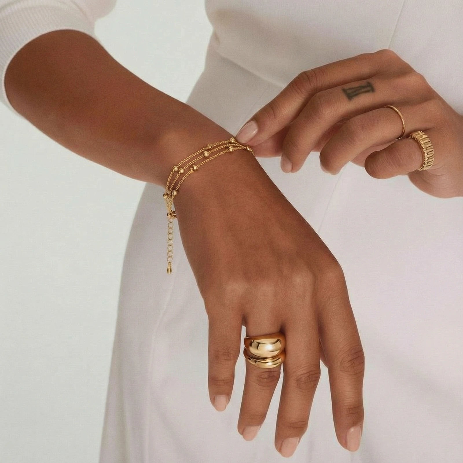Close-up of a hand wearing gold jewelry on a plain background