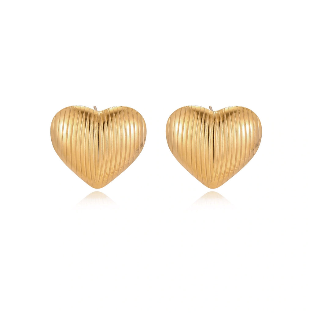 Gold heart-shaped stud earrings with parallel ridged texture on cream background