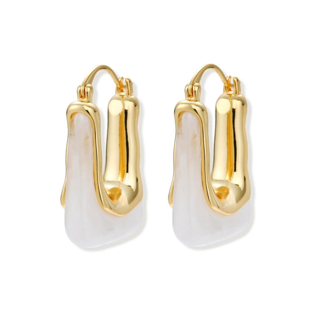 Sculptural gold-plated hoop earrings with flowing curved design and lever-back closure on cream background.