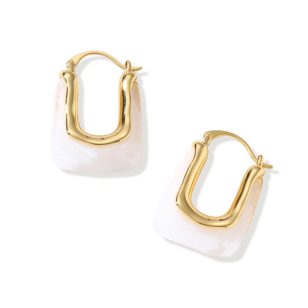 Sculptural gold-plated hoop earrings with flowing curved design and lever-back closure on cream background.