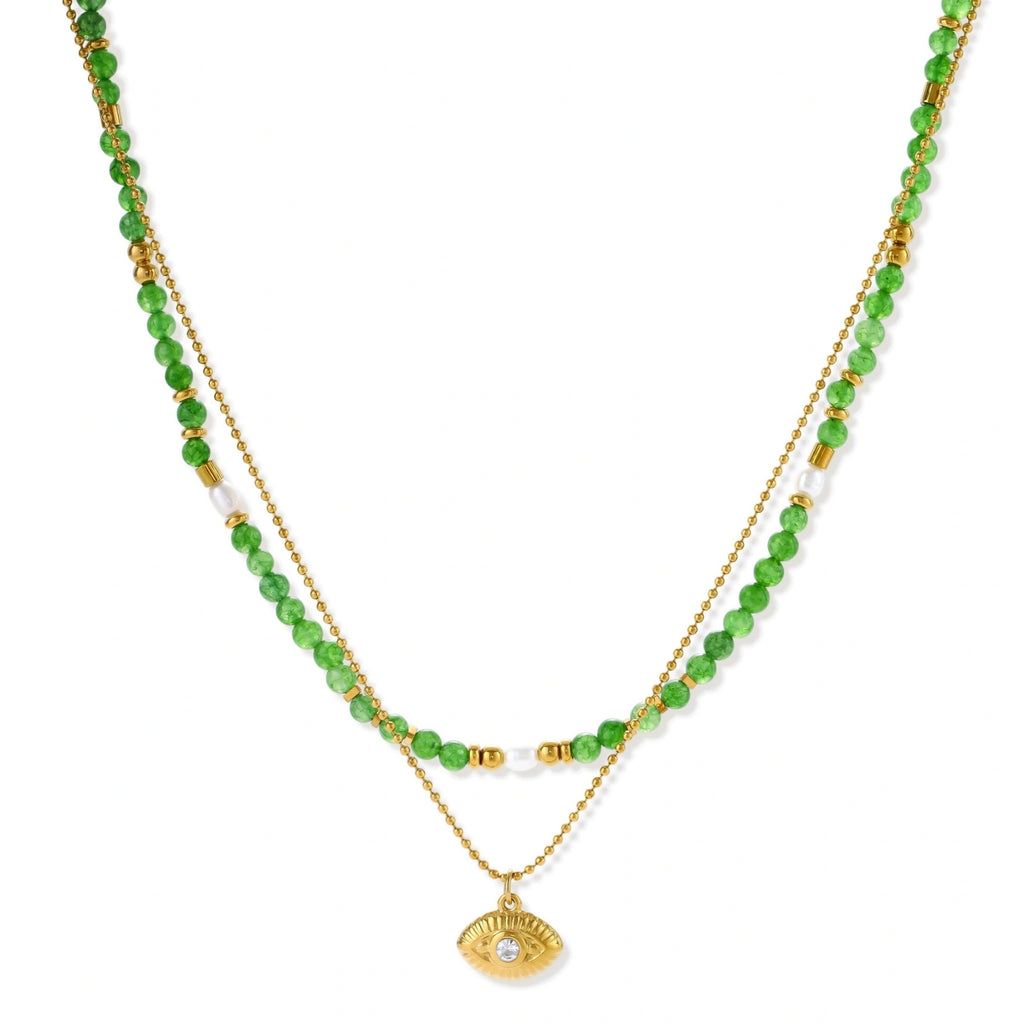 Layered necklace with green stone beads, gold spacers, white accents, and protective eye pendant on cream background.