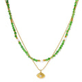 Layered necklace with green stone beads, gold spacers, white accents, and protective eye pendant on cream background.
