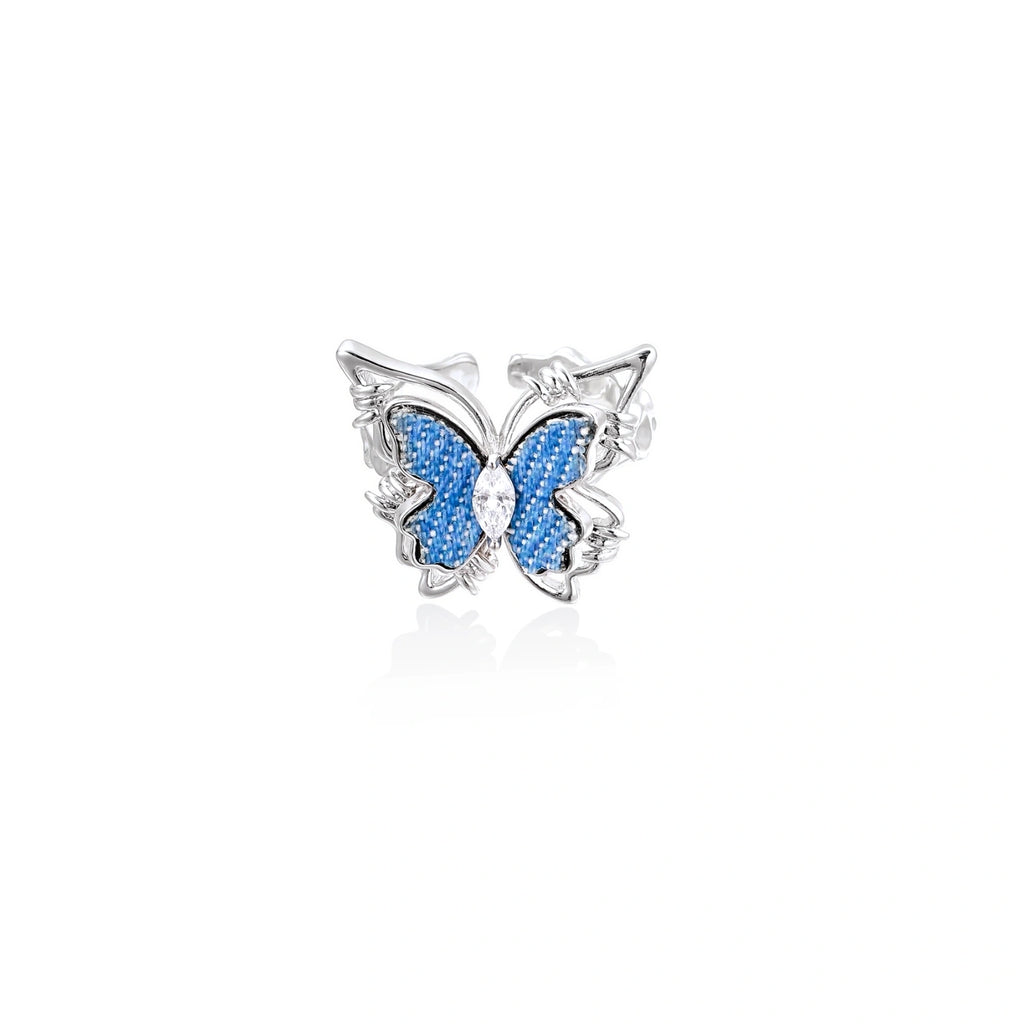Silver-toned ring with blue denim butterfly wings, marquise zirconia center, and ornate scrollwork band on white background