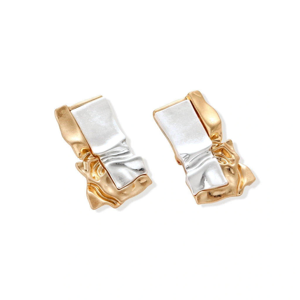Close-up of avant-garde sculptural earrings with flowing liquid metal design in gold and silver tones on white background.