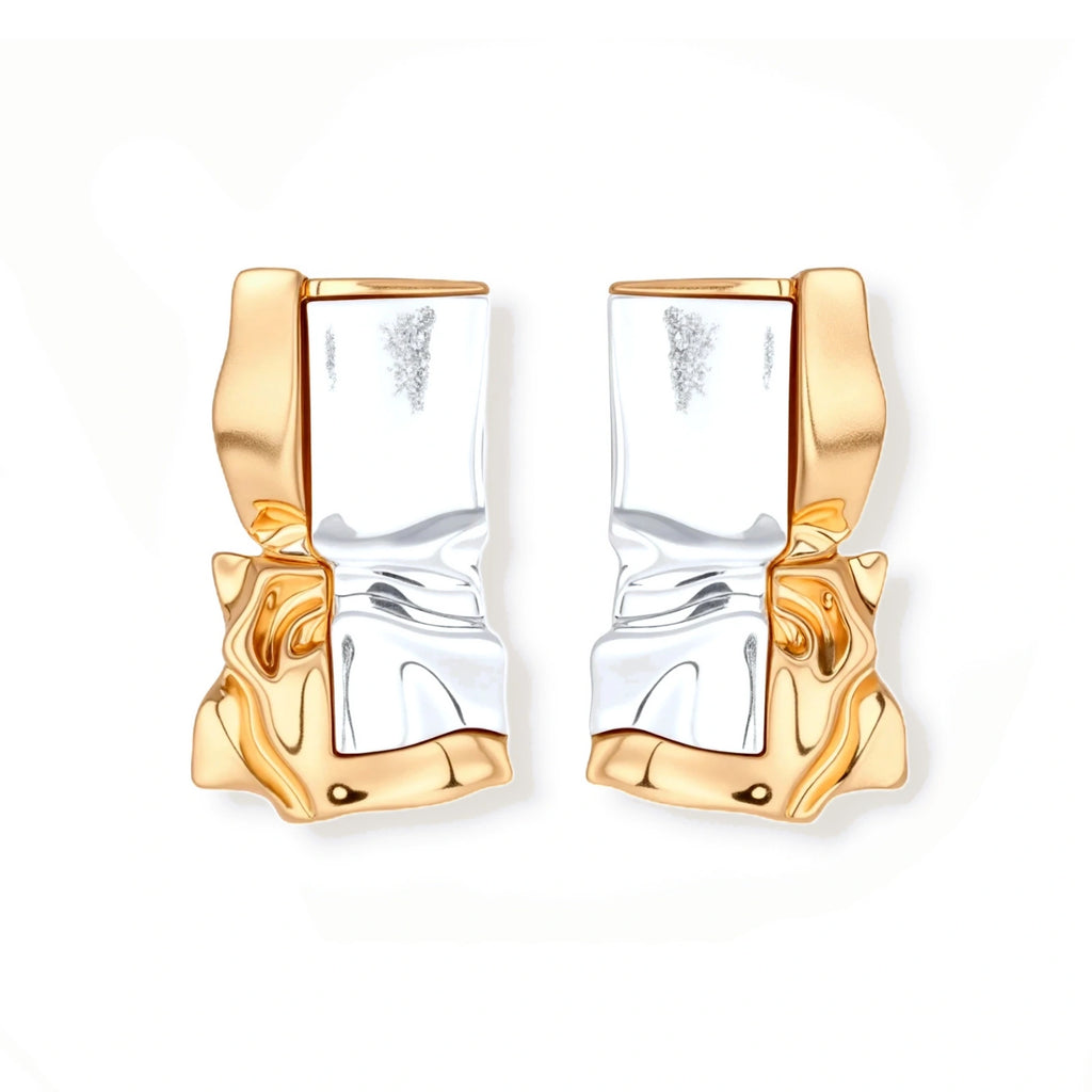 Close-up of avant-garde sculptural earrings with flowing liquid metal design in gold and silver tones on white background.