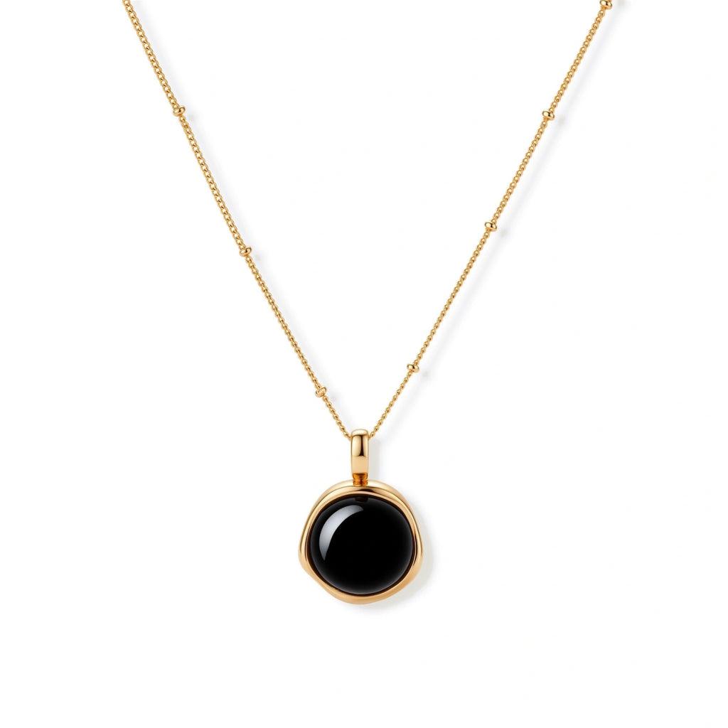 Circular black agate pendant on gold-plated sterling silver chain against cream background, showing modern minimalist design.