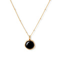 Circular black agate pendant on gold-plated sterling silver chain against cream background, showing modern minimalist design.