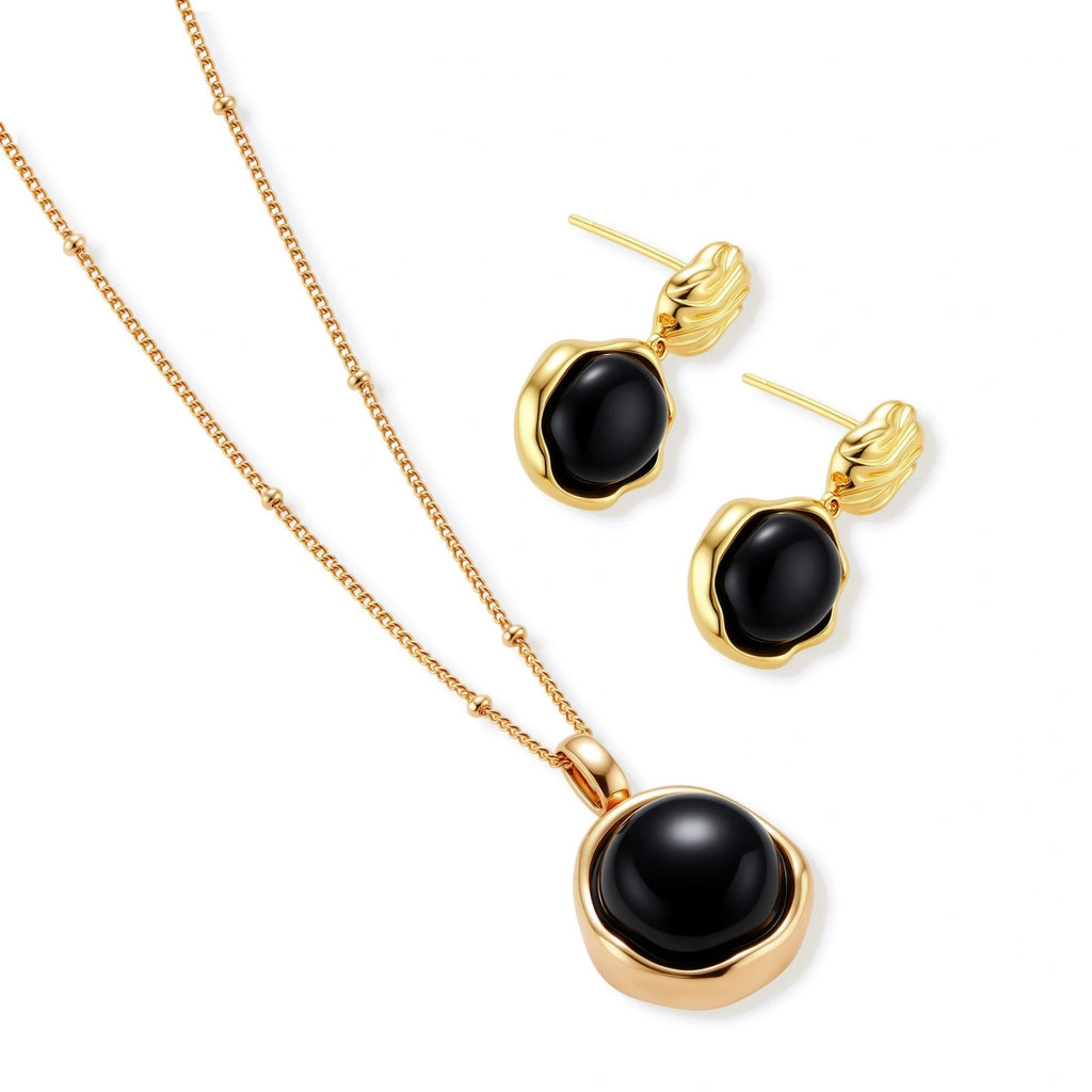 Circular black agate pendant on gold-plated sterling silver chain against cream background, showing modern minimalist design.