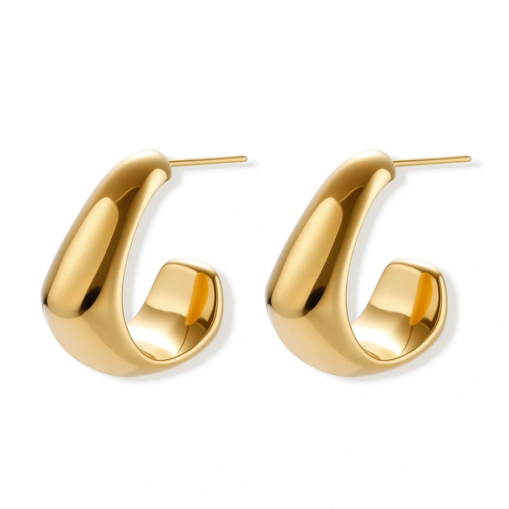 Close-up of curved gold-plated huggie earrings with sculptural design on white background, showing polished finish.