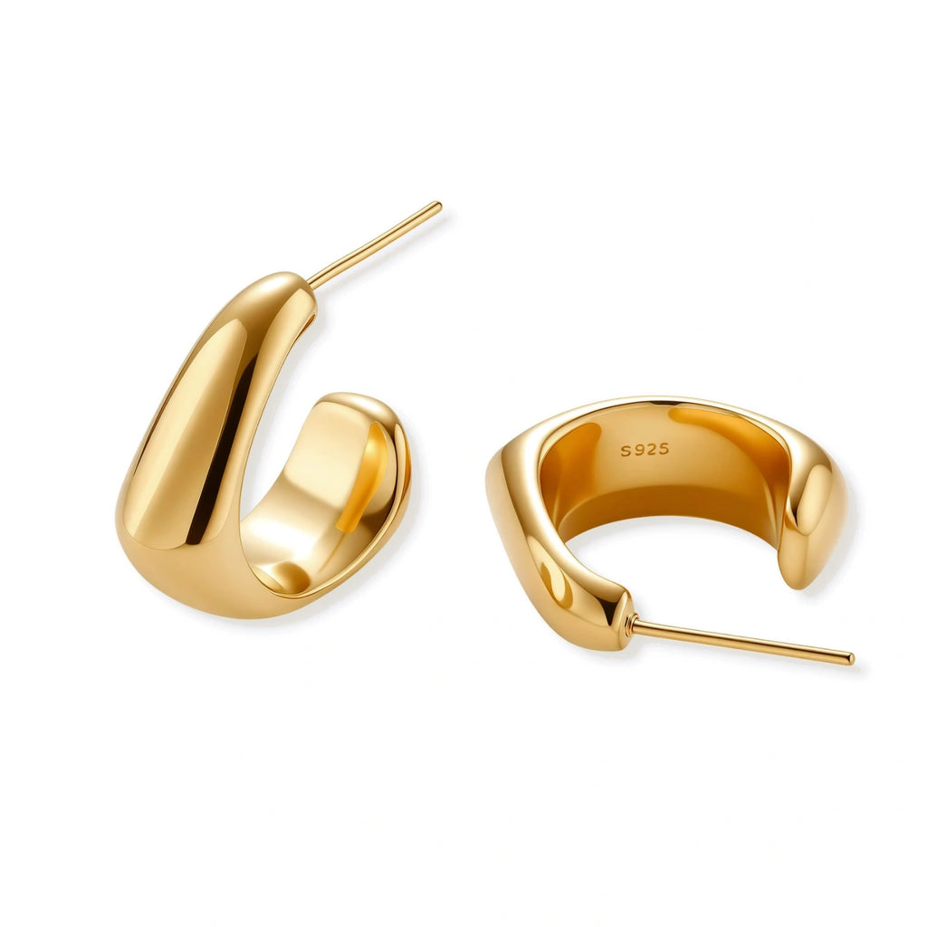 Close-up of curved gold-plated huggie earrings with sculptural design on white background, showing polished finish.
