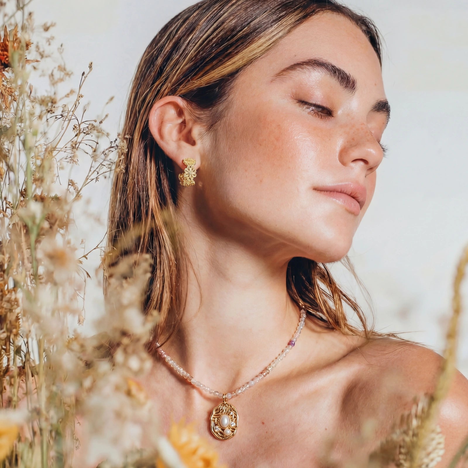 Woman wearing gold earrings and necklace among dried plants