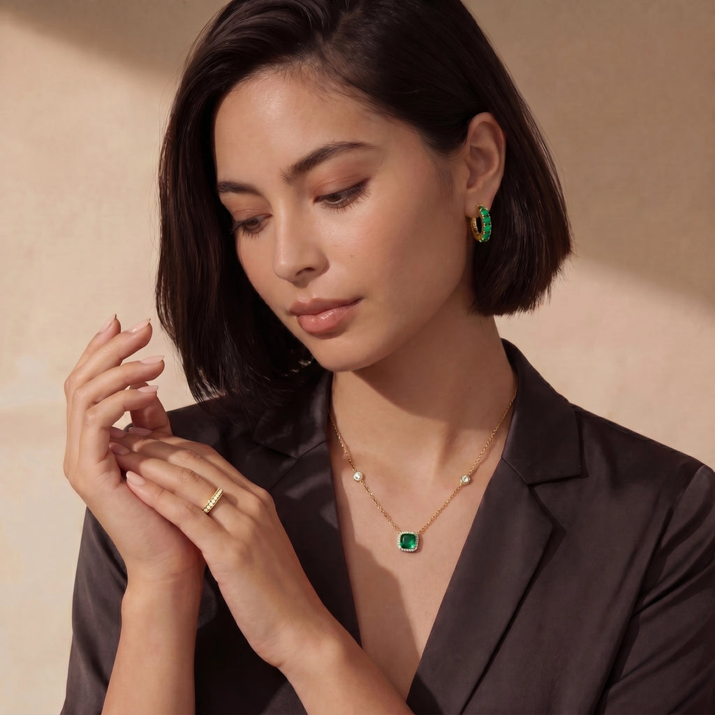 Woman wearing a gold necklace with a green gemstone and earrings against a beige background