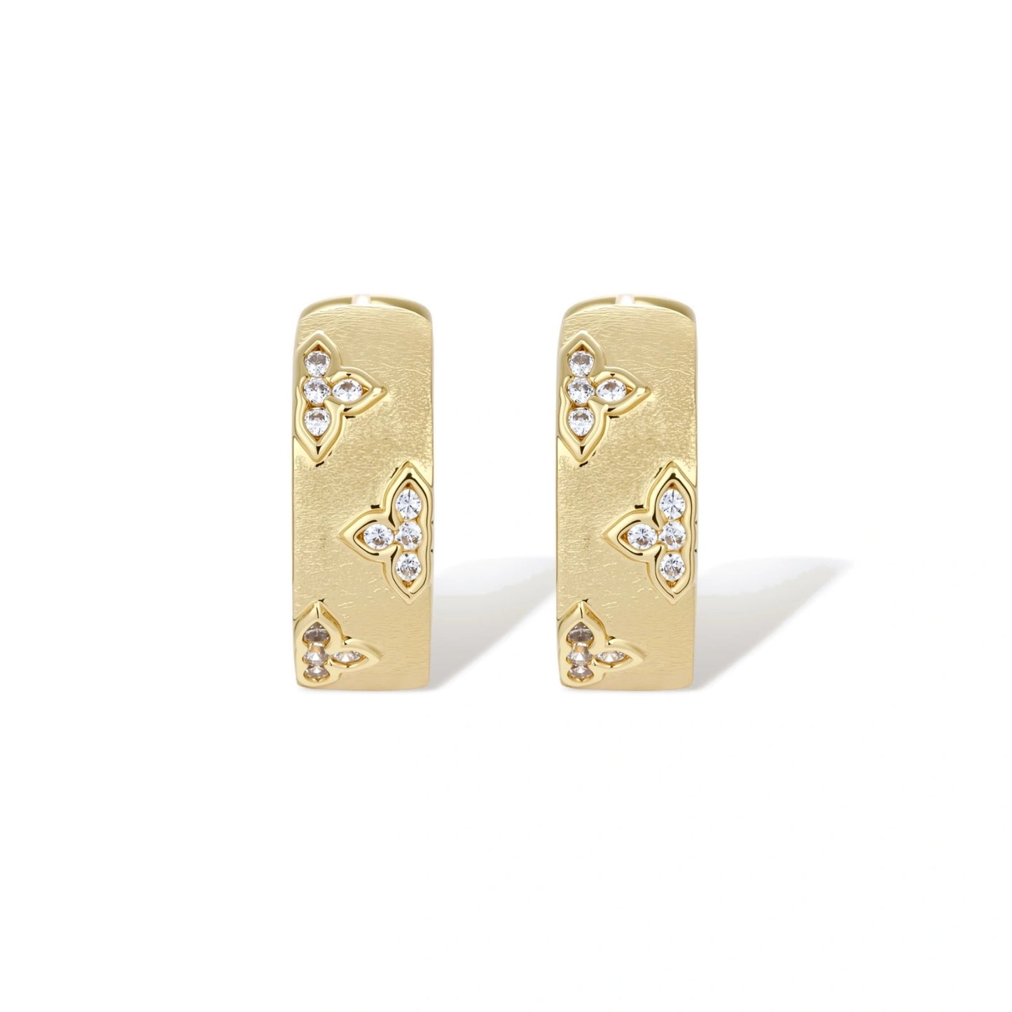 Gold-plated hoop earrings with textured surface and raised floral motifs set with clear zirconia stones on cream background.