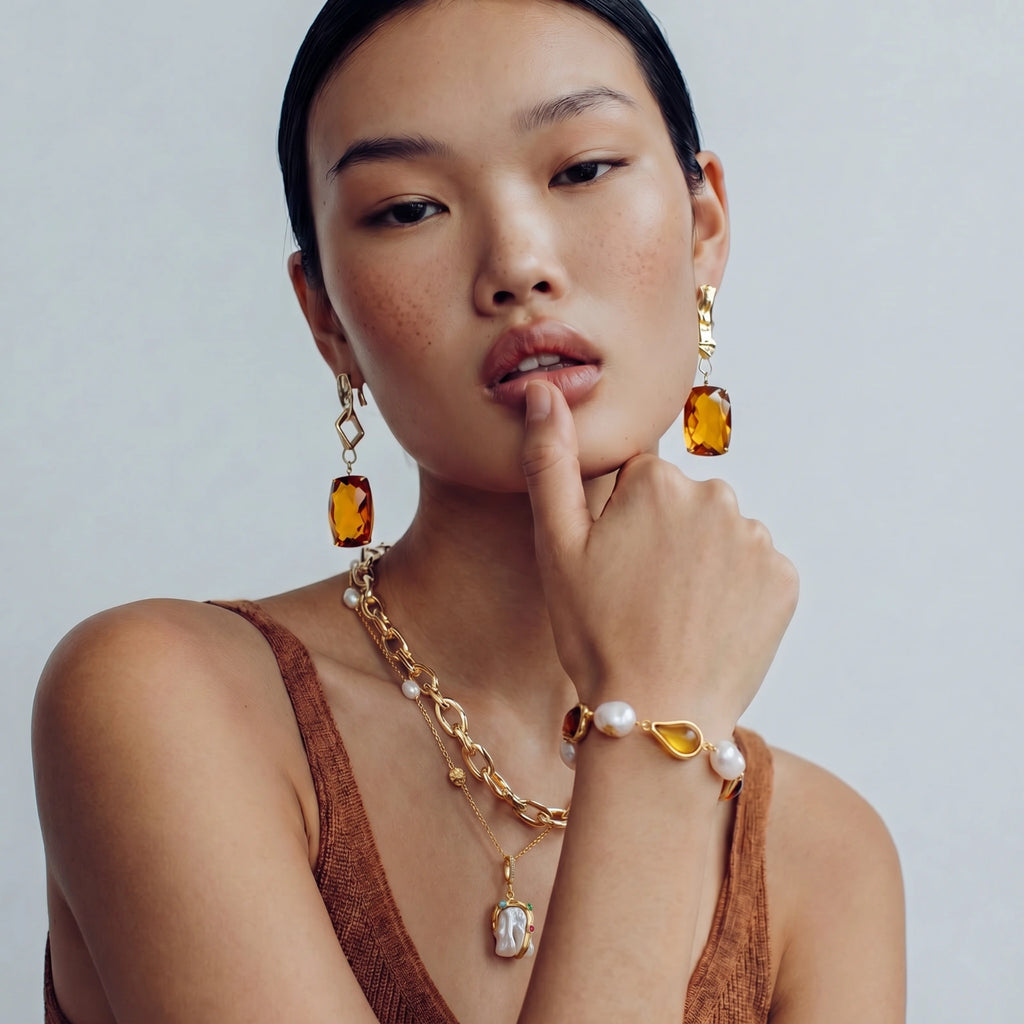 Woman wearing gold jewelry with amber stones on a plain background