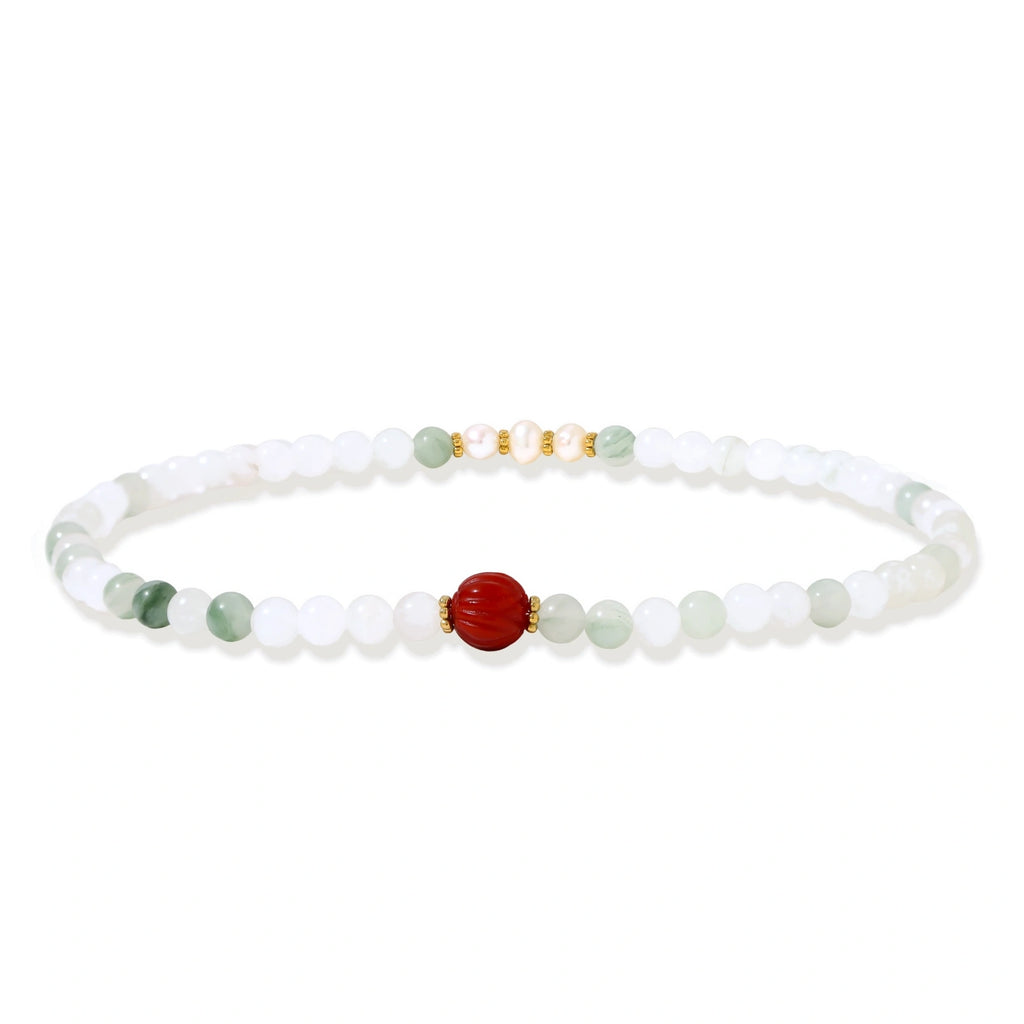 Three layered white beaded bracelets with carved orange agate lotus centerpiece and freshwater pearls on cream background.