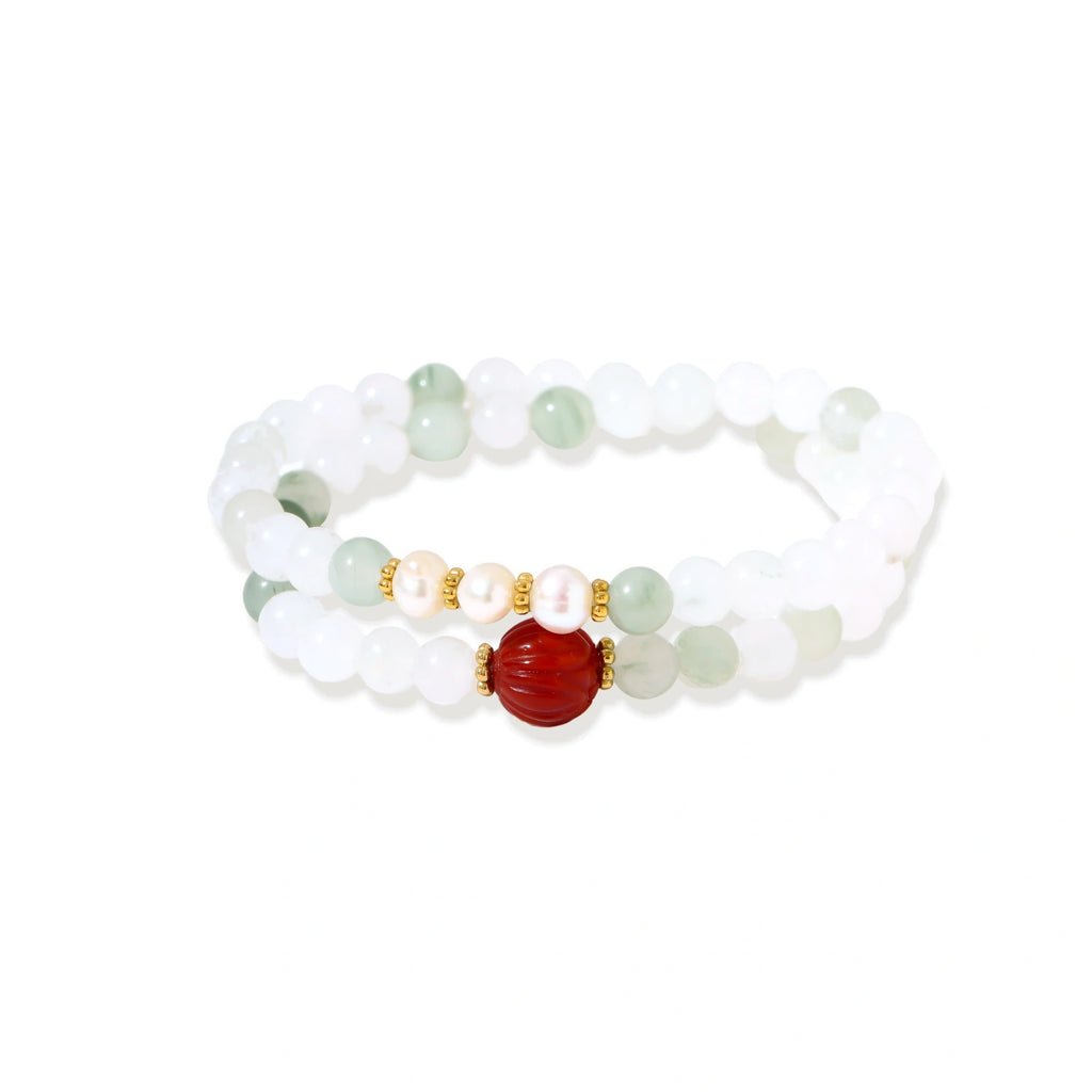 Three layered white beaded bracelets with carved orange agate lotus centerpiece and freshwater pearls on cream background.