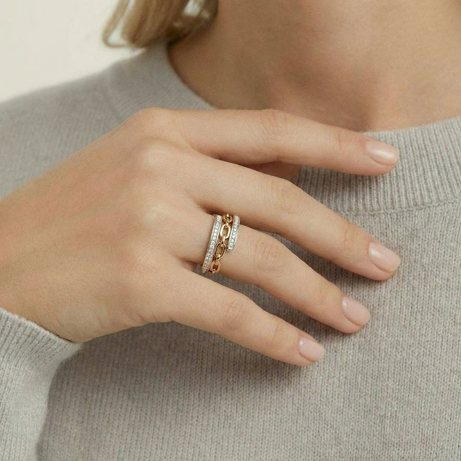 Hand wearing two gold rings on a neutral background
