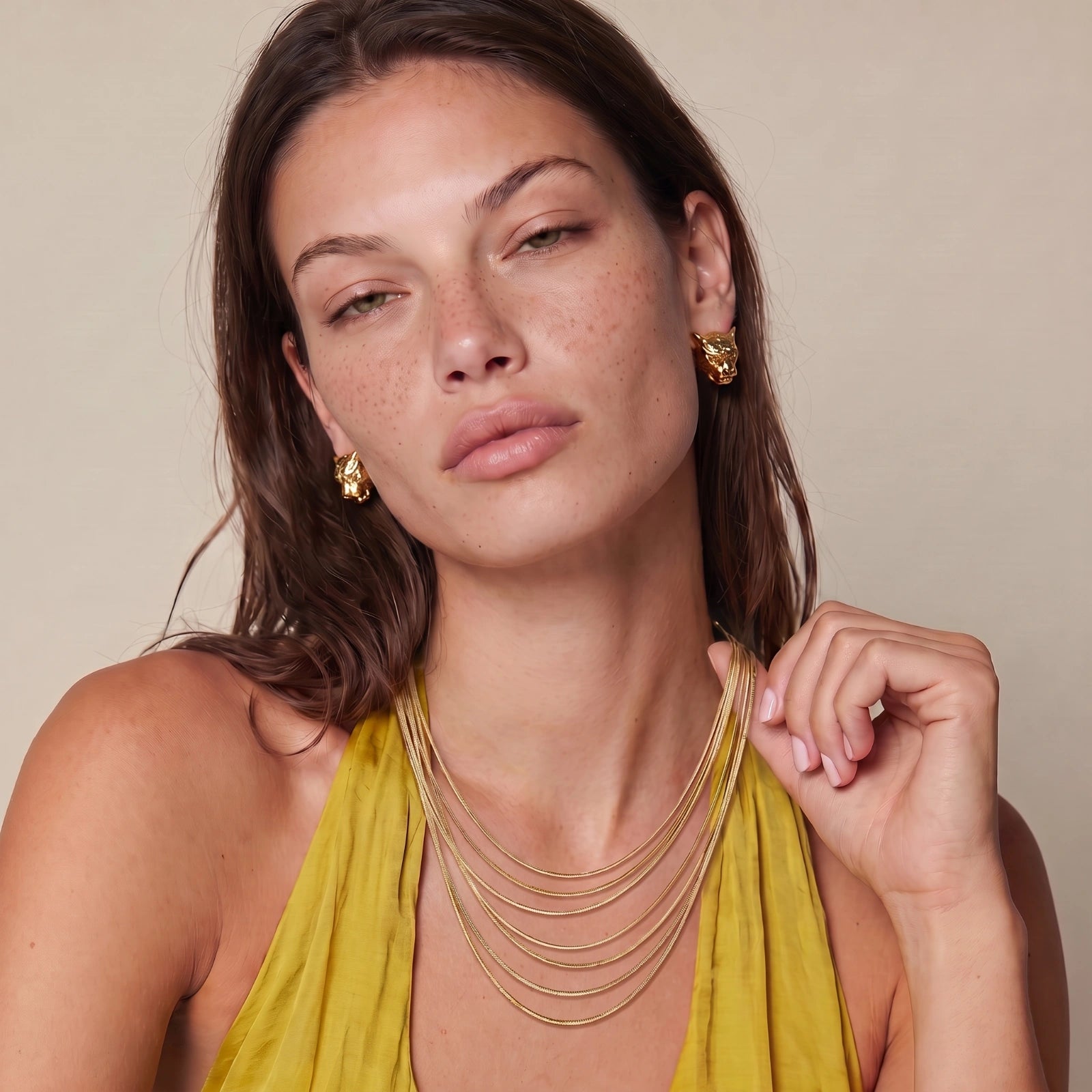 A woman in a green blouse wearing golden earrings and a layered gold necklace.