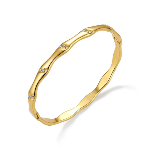 Gold-toned wavy bangle with bamboo-style segments and CZ crystal clusters on cream background. 18K plated stainless steel.