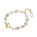 Bracelet with cloudy quartz beads, freshwater pearls, and gold-wrapped baroque pearl centerpiece on white background.