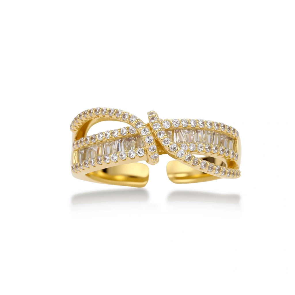 Close-up of gold-plated adjustable ring with crossing bands and sparkling zirconia stones on white background.